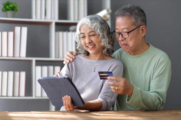 Coppia anziana felice in pensione a casa Coppia pensionata felice con carta di credito che compra online su tablet digitali