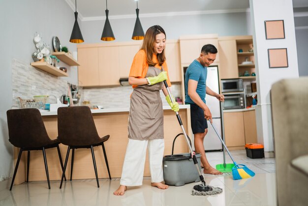 Coppia asiatica che fa insieme le faccende domestiche lavando e spazzando il pavimento