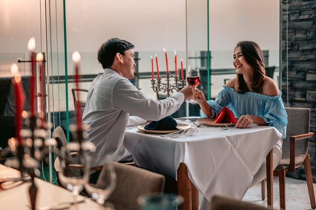 Coppia asiatica con bicchieri di vino che hanno una romantica cena a lume di candela in tavola al ristorante hotelVacationDinnerCoppia d'amore e concetto di coppia dolce