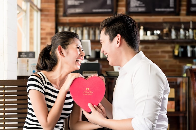 Coppia asiatica, donna e uomo, avendo data nella caffetteria con cuore rosso, festeggia l'anniversario