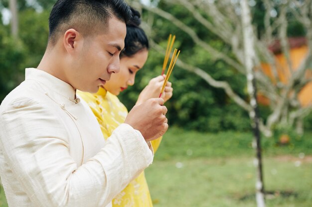 Coppia asiatica in costumi tradizionali che prega con bastoncini di incenso in mano