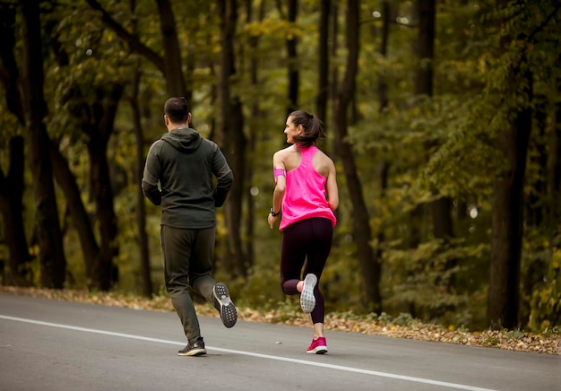 Coppia atletica che corre insieme sul sentiero nel bosco in autunno