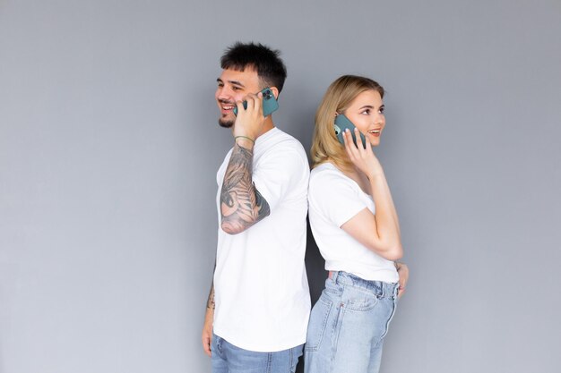 Coppia attraente che parla sui loro smartphone isolati su sfondo grigio