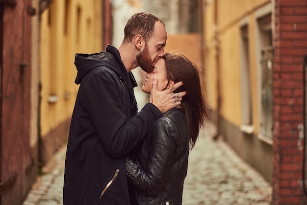 Coppia attraente, uomo barbuto e ragazza bruna che si baciano fuori dalla vecchia strada europea su uno sfondo.