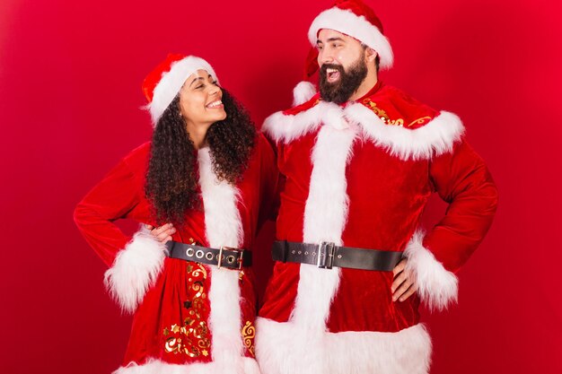 Coppia brasiliana vestita per natale babbo natale mummia claus donna nera e uomo caucasico che si guardano l'un l'altro