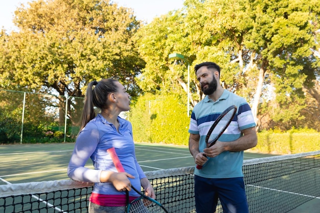 Coppia caucasica che gioca a tennis parlando sul campo da tennis all'aperto