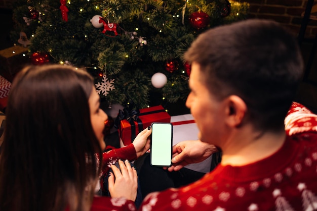 Coppia caucasica che utilizza lo smartphone per la videochiamata natalizia con schermo verde mock up natale