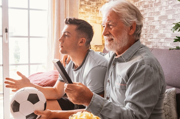 Coppia caucasica di fan di calcio del ragazzo e del nonno senior che guardano una partita di calcio in tv seduti su un comodo divano in soggiorno