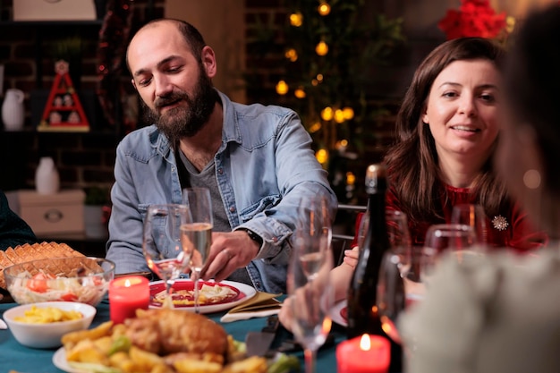 Coppia che celebra il natale con la famiglia, parlando a tavola festiva, mangiando un pasto tradizionale per le vacanze invernali, bevendo spumante. Festa di Natale a casa festa, moglie e marito in chat