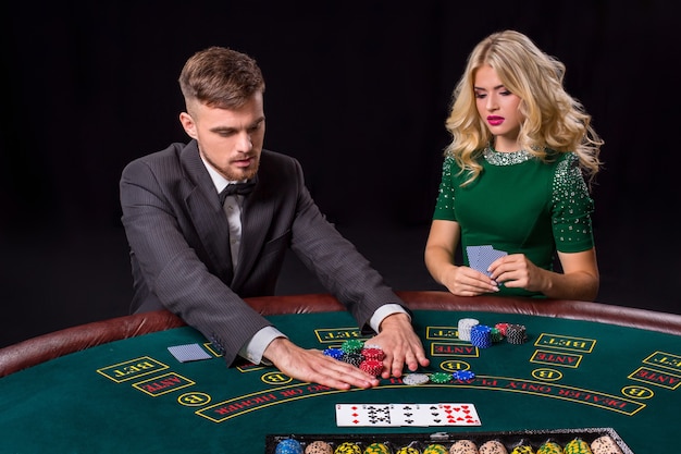 Coppia che gioca a poker al tavolo verde. La ragazza bionda e un ragazzo in giacca e cravatta. fiches per scommesse all-in