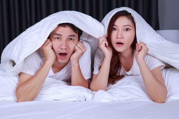 coppia che guarda film spaventato sotto la coperta sul letto