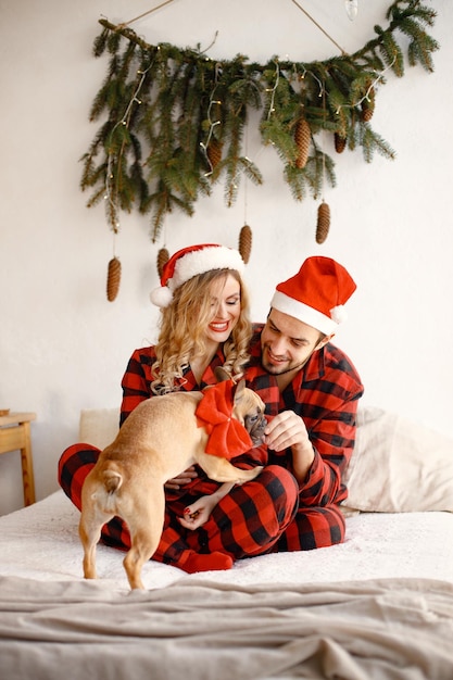 Coppia che indossa un pigiama rosso plaid natalizio con cane sul letto