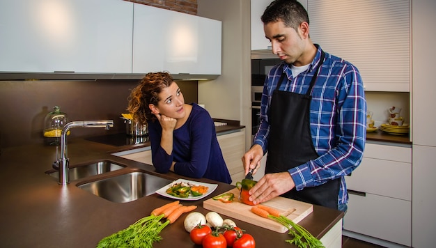 Coppia che parla in cucina mentre il marito taglia le verdure per preparare il cibo
