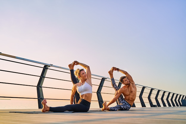 Coppia che pratica yoga insieme sulla natura all'aperto esercizi mattutini all'alba
