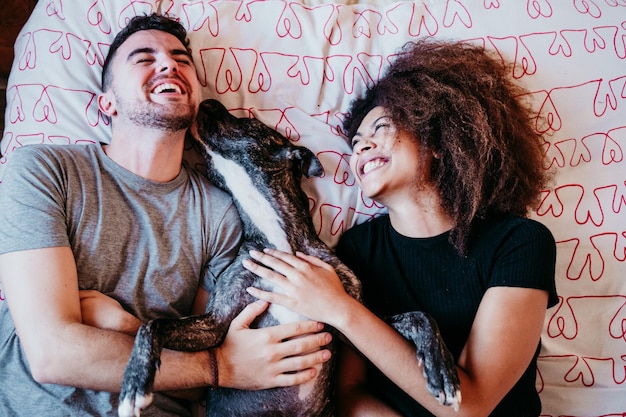 Coppia che ride sdraiata sul letto con il cane a casa
