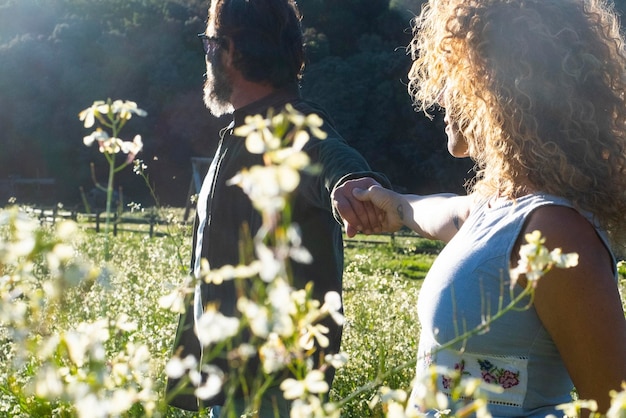 Coppia che si tiene per mano e cammina insieme nel parco dei fiori di prato in fiore Concetto di stile di vita sano e relazione Persone che si godono la natura e la destinazione del viaggio Tempo libero stile di vita uomo e donna