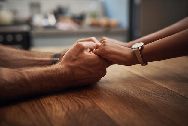 Coppia che si tiene per mano in supporto al dolore e alla guarigione insieme su un tavolo di legno a casa Primo piano di un partner premuroso nel dolore a causa del cancro ed esprime sentimenti di compassione in una casa