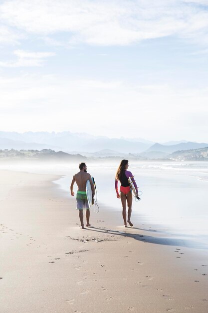 Coppia che trasporta tavole da surf che camminano sulla spiaggia