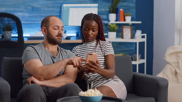 Coppia che usa il telefono mentre è seduta sul divano con i popcorn