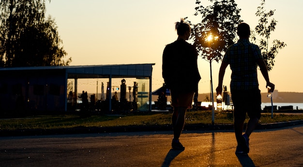 Coppia con bottiglia e bevande che camminano al tramonto. Foto di alta qualità