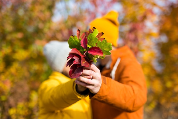 Coppia con bouquet di foglie autunnali che si baciano nella foresta autunnale o nel parco