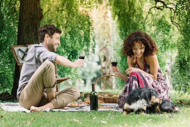 Coppia con cane che fa un picnic in un parco bevendo vino rosso