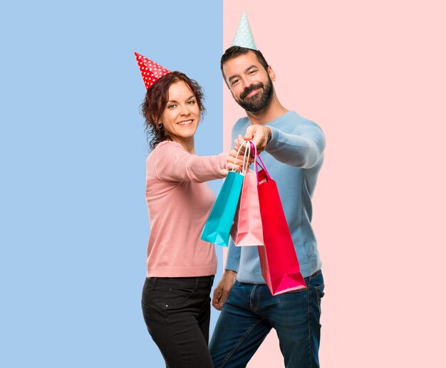 Coppia con cappelli di compleanno e con borse della spesa su sfondo rosa e blu