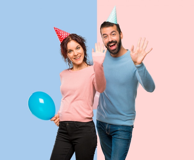 Coppia con palloncini e cappelli di compleanno salutando con la mano con espressione felice