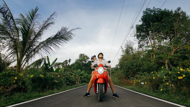 Coppia d'amore su una moto rossa in abiti bianchi per andare in viaggio su strada forestale Due turisti caucasici