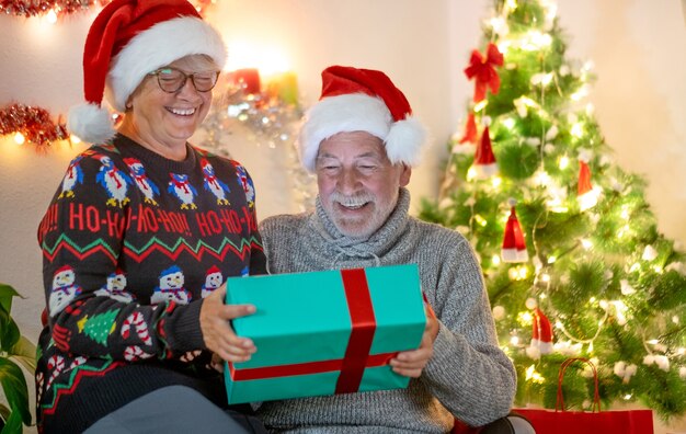 Coppia di anziani che si scambiano regali di Natale a casa con grandi sorrisi