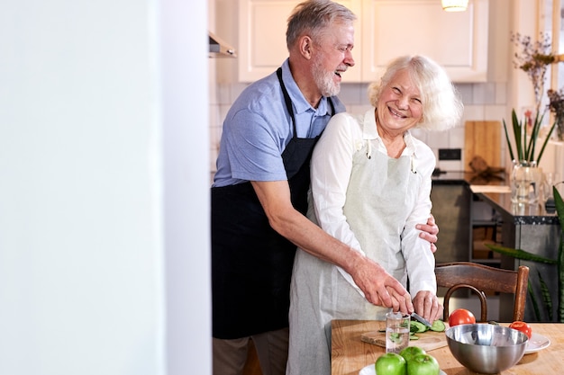 Coppia di anziani intagliare verdure insieme, uomo dai capelli handsomegray aiutare la moglie a cucinare