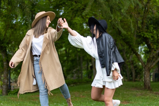 Coppia di belle donne in cappelli che ballano e si divertono tenendosi per mano nel parco