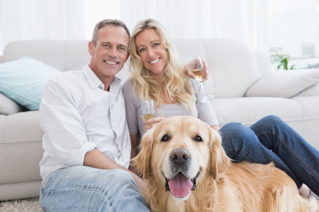 Coppia di bere champagne con il loro cane di fronte a loro a casa in salotto