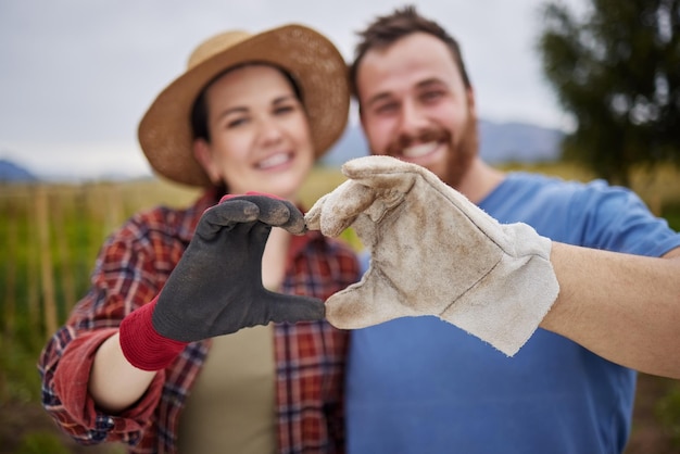 Coppia di coltivatori o giardinieri che mostra il segno del cuore d'amore con le mani all'aperto in una fattoria biologica o sostenibile Attivisti felici ed entusiasti sostengono la sostenibilità o l'agricoltura biologica