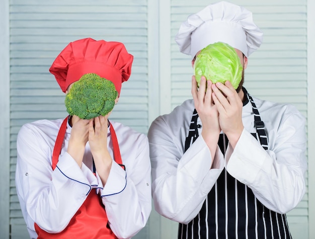 Coppia di cuochi tengono cavoli e broccoli davanti al viso Concetto di cibo sano Coppia che cucina un pasto vegetariano sano Famiglia vegetariana Nutrizione vegetariana e dieta vegetale Dieta nella loro mente