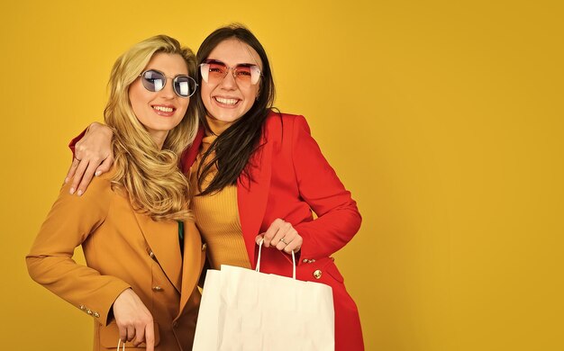 Coppia di donne andare a fare shopping due donne portano borse della spesa grandi saldi e venerdì nero colori autunnali luminosi autunno e primavera stile alla moda look alla moda per ogni stagione amicizia e sorellanza