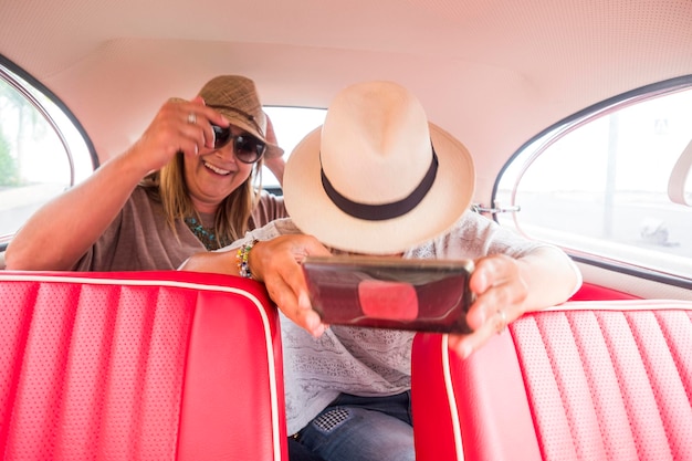 Coppia di donne caucasiche amiche che si godono un'auto d'epoca rossa che si fa selfie con uno smartphone moderno contrasta con le nuove cose legate alla tecnologia, divertimento e godimento del concetto