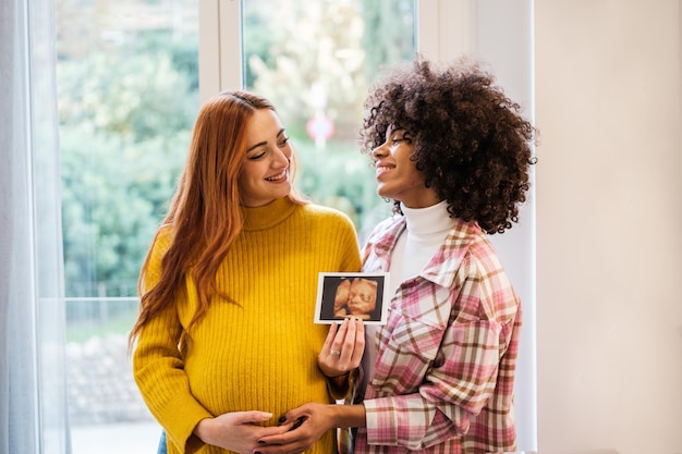 Coppia di donne che presentano la foto della gravidanza orgogliose del loro futuro Integrazione dell'orgoglio di maternità del concetto