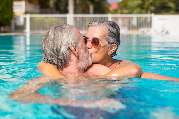 Coppia di due anziani felici che si divertono e si divertono insieme in piscina sorridendo e giocando. Gente felice che si gode l'estate all'aperto nell'acqua