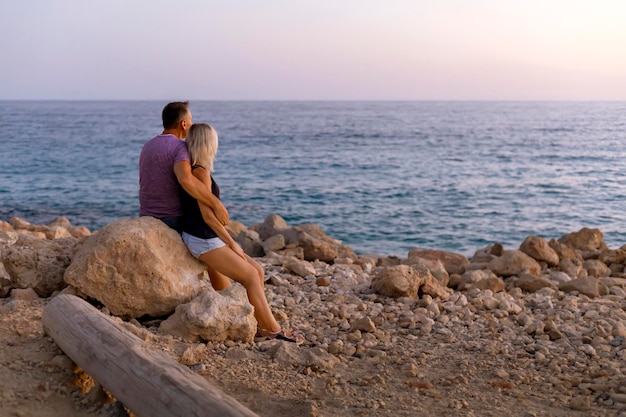 Coppia di due persone mature felici in spiaggia guardando il mare al tramonto. viaggiare per le vacanze estive.