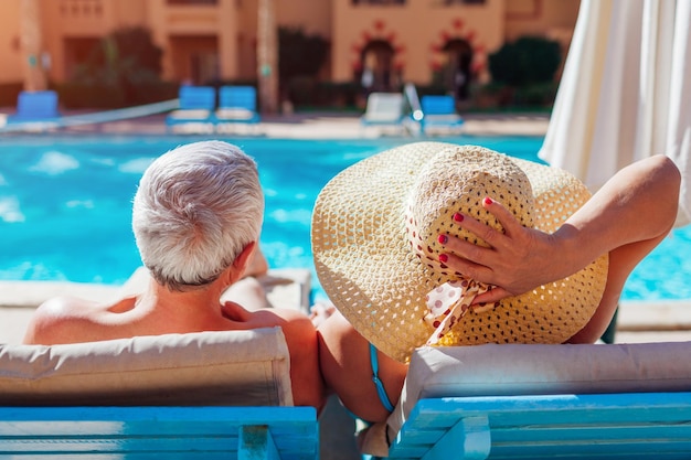 Coppia di famiglia anziana che si rilassa in piscina sdraiata su chaiselongues Persone che si godono le vacanze estive