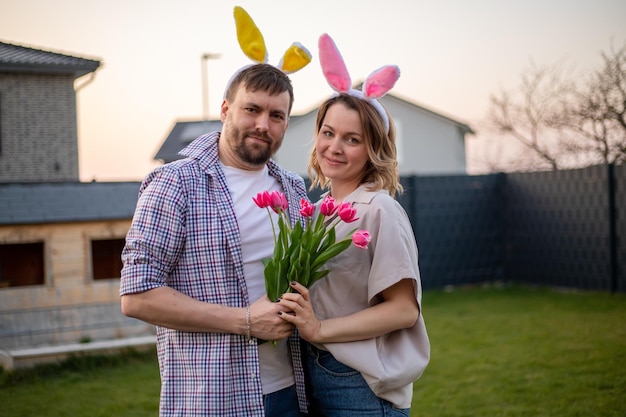 Coppia di famiglia che indossa orecchie da coniglio per celebrare la Pasqua il marito regala a sua moglie tulipani