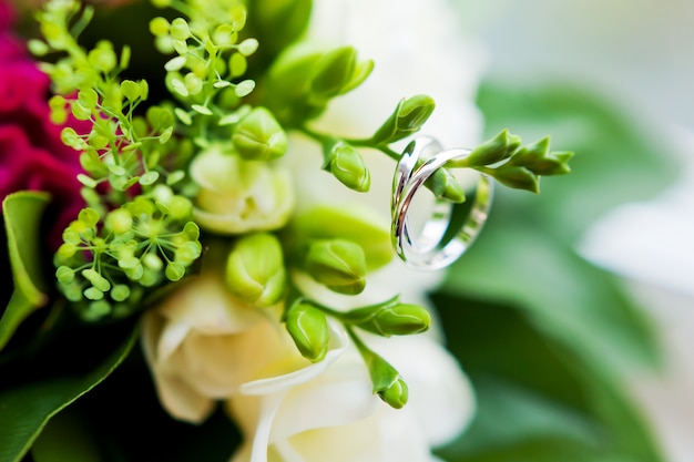 Coppia di fedi nuziali dorate all'interno di un bouquet. Accessorio tradizionale della sposa. Composizione floreale con fiori rossi di celosia.
