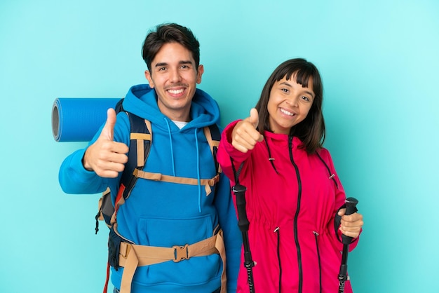 Coppia di giovani alpinisti isolati su sfondo blu dando un pollice in alto gesto perché è successo qualcosa di buono