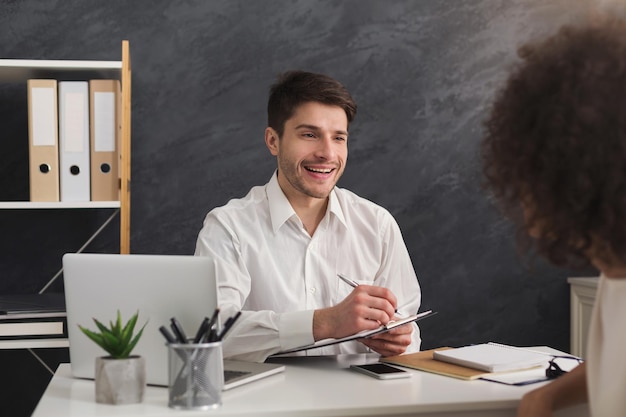 Coppia di giovani colleghi che lavorano in un ufficio moderno. Uomo allegro che intervista una candidata, copia spazio