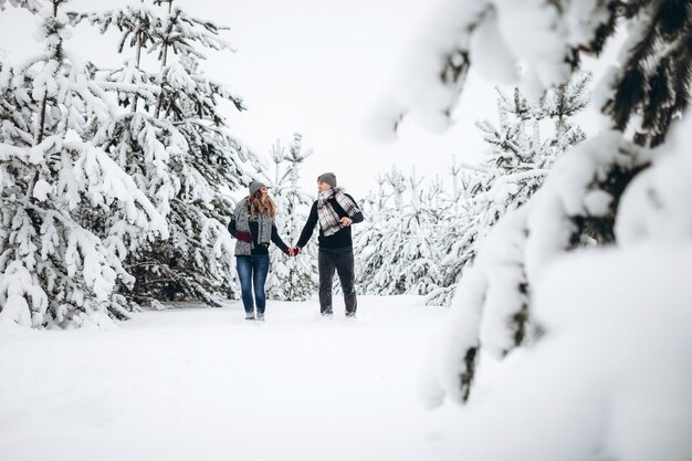 Coppia di innamorati attraversa un bosco innevato in inverno in un maglione e una sciarpa e sorride