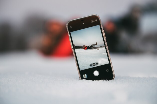 Coppia di innamorati che si abbracciano e giocano mentre si prende selfie sul cellulare posizionato sulla neve in campagna