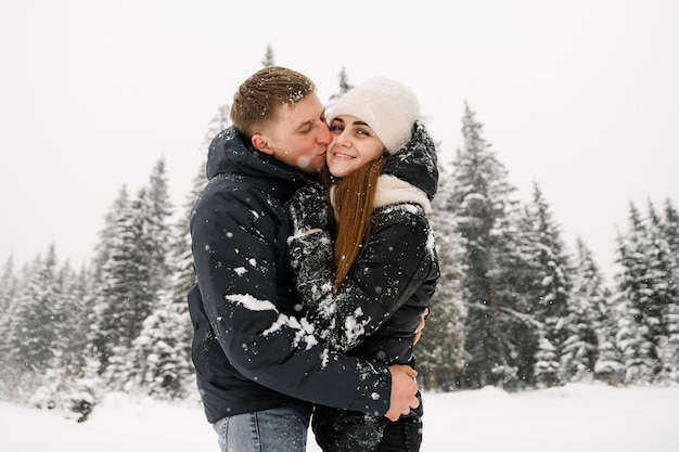 Coppia di innamorati coccole durante una passeggiata invernale. Giovane famiglia che si diverte nella foresta gelida. Appuntamento romantico nel periodo invernale. Storia d'amore invernale