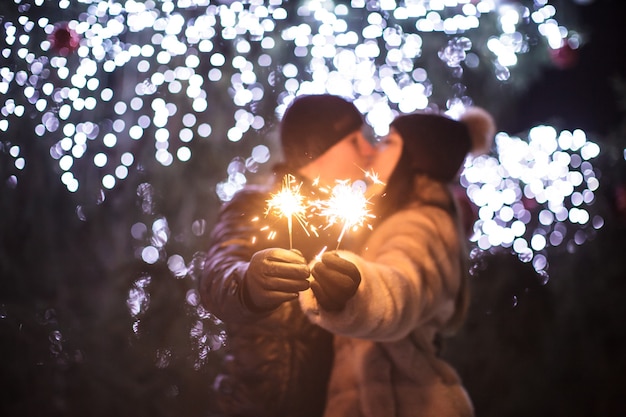 Coppia di innamorati con luce scintillante del Bengala che si bacia vicino a un albero di Natale