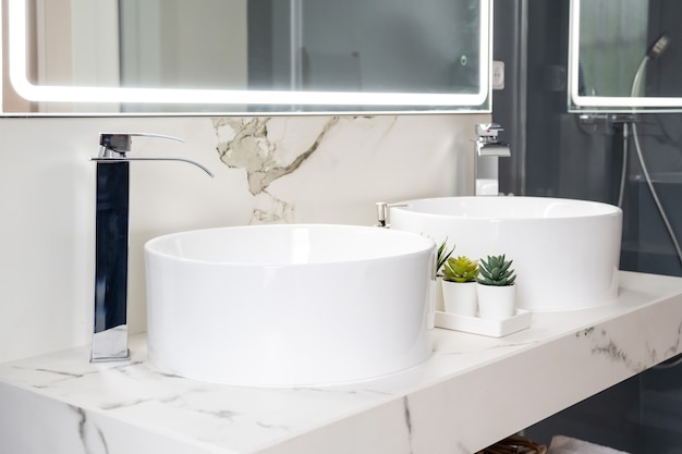Coppia di lavabi in ceramica all'interno di un bagno moderno e luminoso con uno specchio con luce